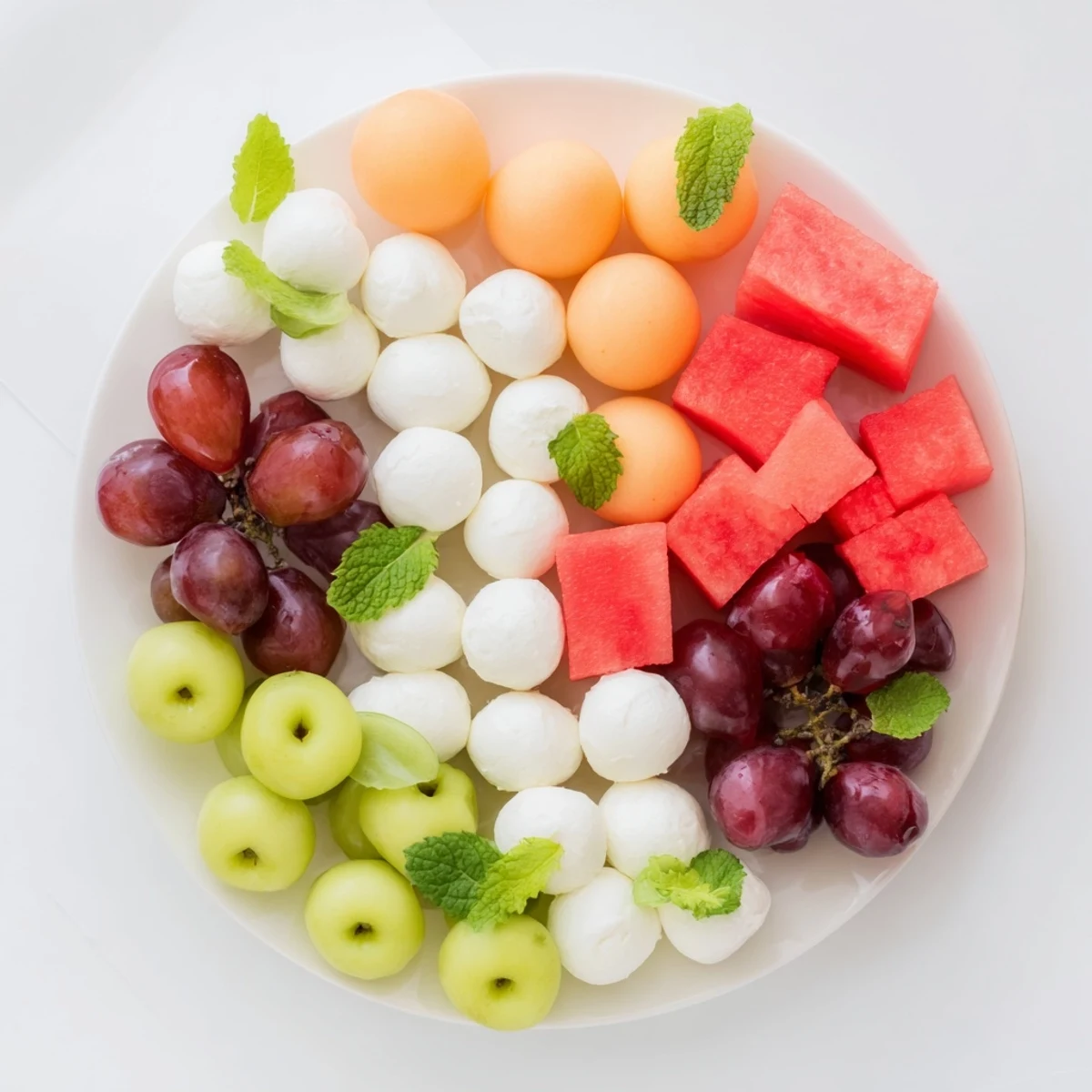 Vibrant polka dot platter showcasing colorful melon balls, grapes, cheeses, and olives; perfect for parties.