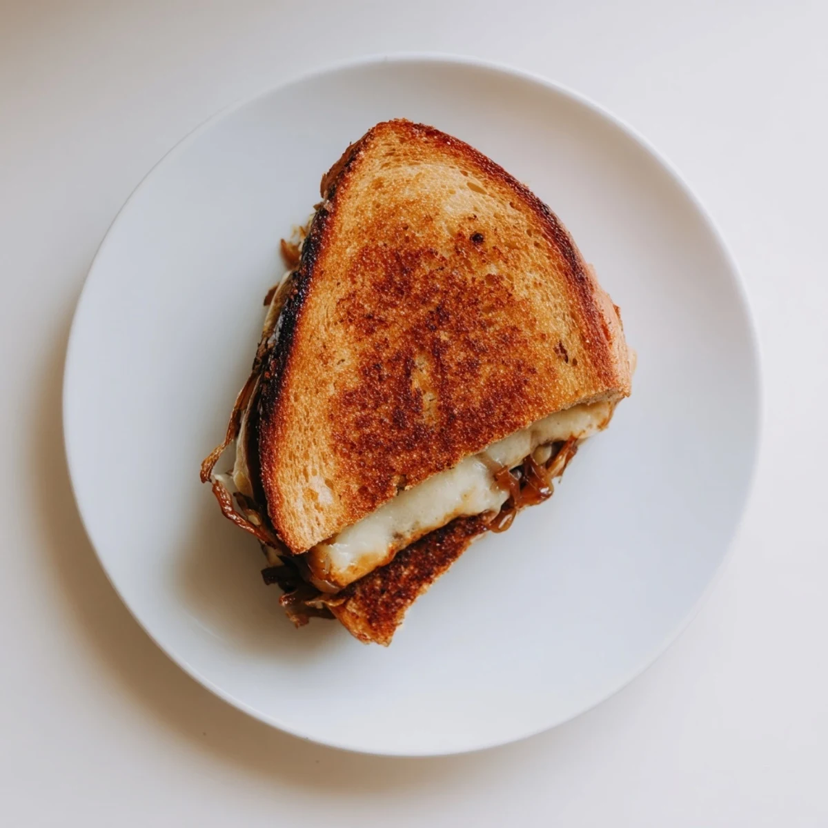 Golden-brown slices of Caramelized Onion & Gruyère Grilled Cheese steam on a cutting board, revealing layers of gooey melted cheese and sweet, tender onions.  