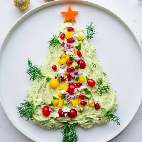 Creamy whipped avocado Christmas tree dip decorated with colorful tomatoes and peppers, perfect holiday appetizer.