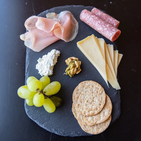 A compact Charcuterie Board for One displays savory meats, cheeses, and grapes for easy enjoyment.