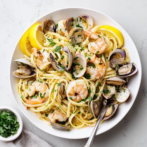 Bright green parsley and lemon wedges garnish a steaming plate of Seafood Linguine, loaded with shrimp, clams, and mussels in a glossy white wine and garlic sauce.  