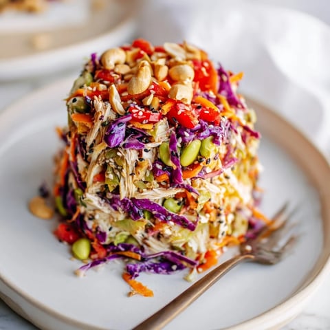 Vibrant Edamame Crunch Chicken Salad in a white bowl, featuring shredded chicken, colorful cabbages, and carrots tossed in a zesty ginger dressing.