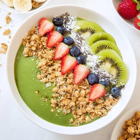 A vibrant green smoothie bowl topped with crunchy granola and fresh fruit like kiwi and strawberries.