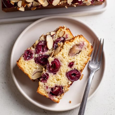 This tender Cherry Almond Loaf Cake showcases halved cherries throughout the golden quick bread.