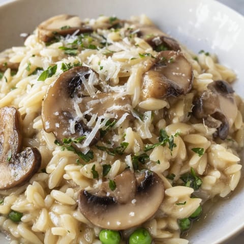 A steaming skillet of orzo mushroom risotto-style with sautéed mushrooms, peas, and a rich, cheesy finish.  