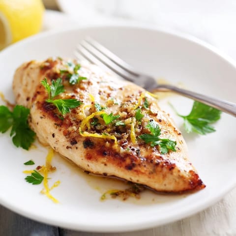 A close-up of tender Lemon Pepper Chicken with fresh parsley garnish, glistening with a zesty, garlicky pan sauce.