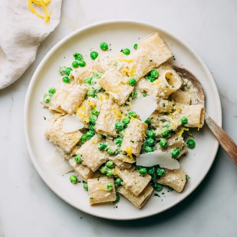 Tender green peas and grated Parmesan add flavor to a bowl of Pea & Lemon Ricotta Pasta, garnished with basil and lemon zest.