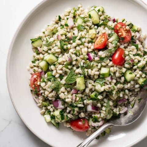 A Mediterranean barley and herb salad featuring crisp cucumbers and red onion, drizzled with lemon dressing and garnished with fresh herbs.