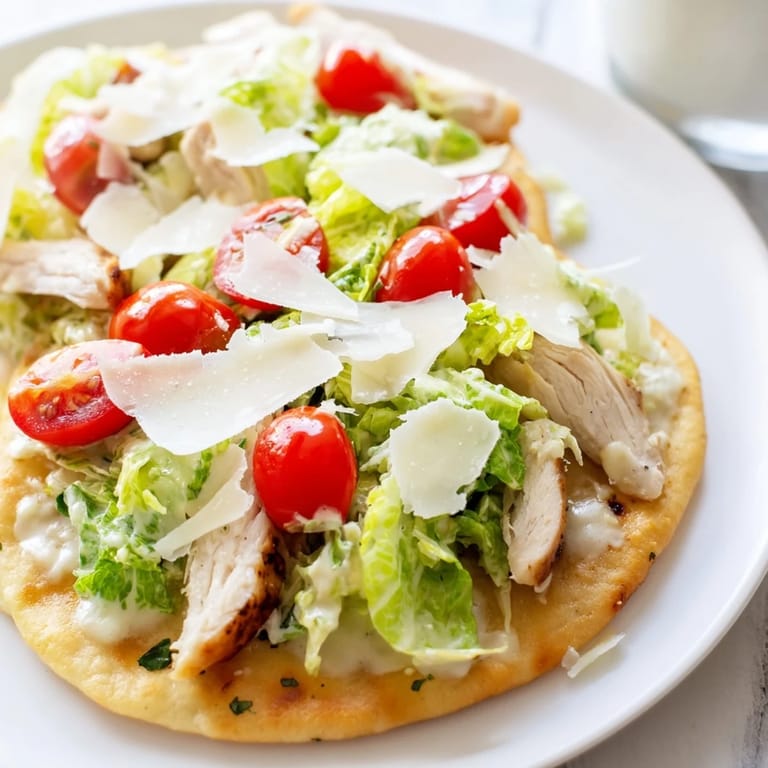 Imagine a golden flatbread spread with juicy grilled chicken, crunchy romaine, and Caesar dressing, garnished with fresh cherry tomatoes and lemon wedges.