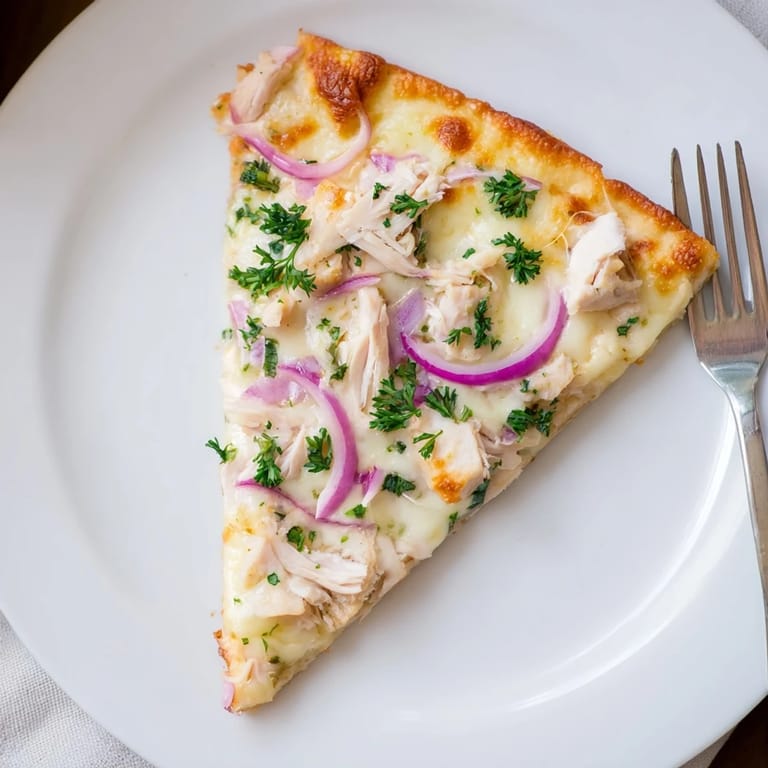 A slice of Chicken Alfredo Pizza being lifted, revealing gooey cheese and a crisp crust.