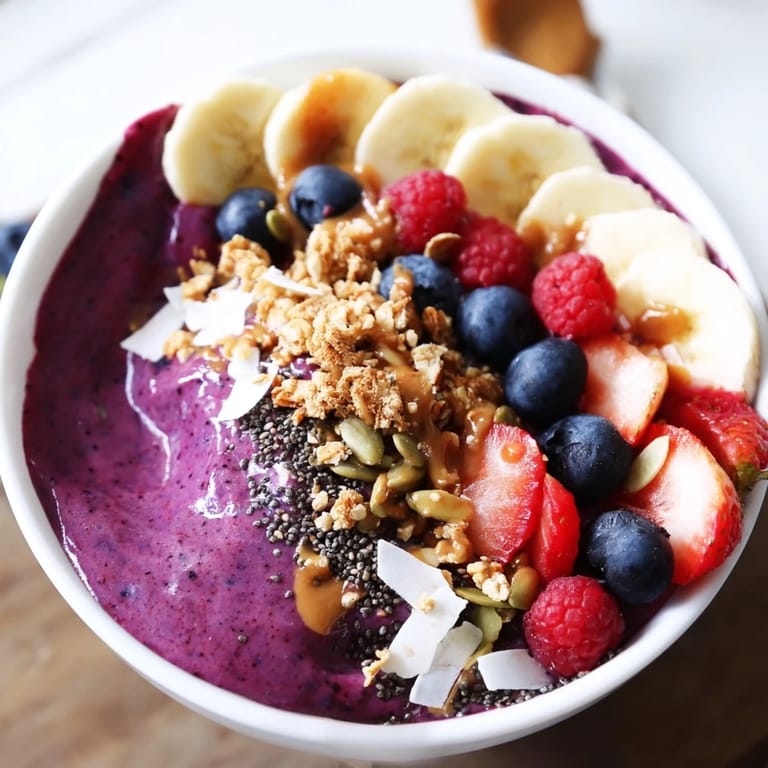 Colorful acai berry smoothie bowl featuring fresh fruit, chia seeds, and granola, served in a white bowl for a healthy, energizing snack.