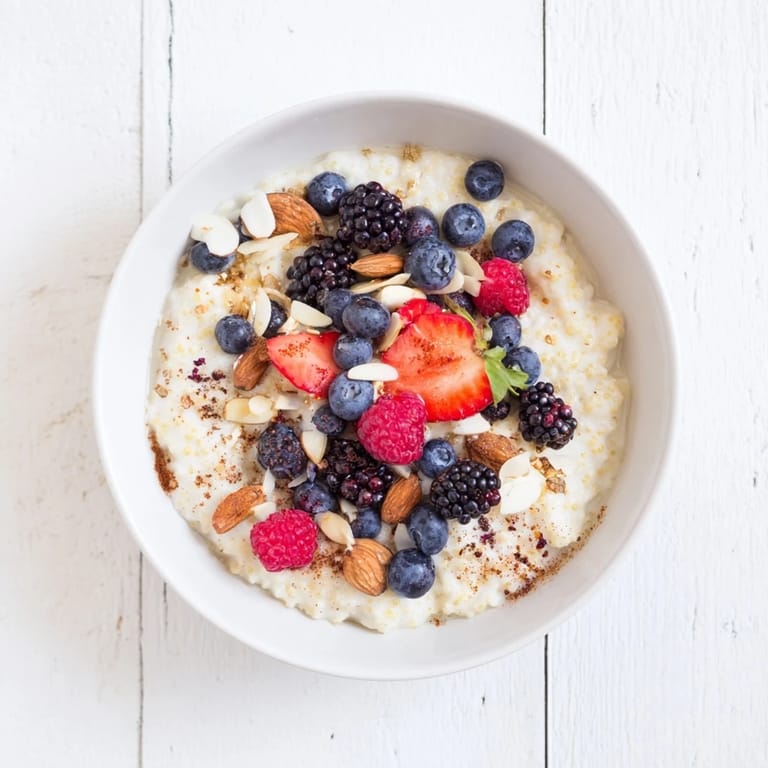 Steaming bowl of homemade millet porridge garnished with raspberries, blueberries, and a drizzle of maple syrup.