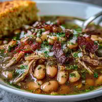 Smoky ham hock and bean soup with tender cornbread, garnished with fresh parsley for a comforting Southern meal.